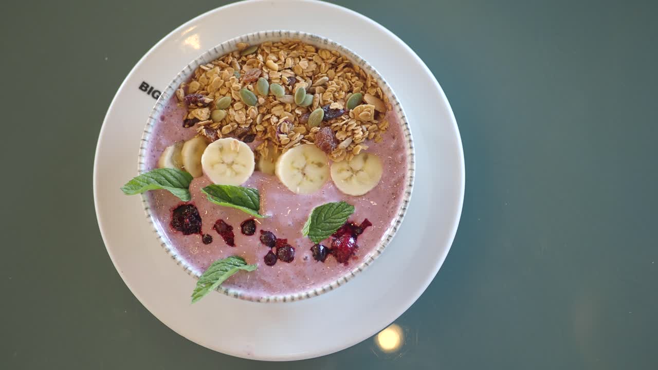 A vibrant smoothie bowl topped with granola, banana slices, berries, and fresh mint leaves