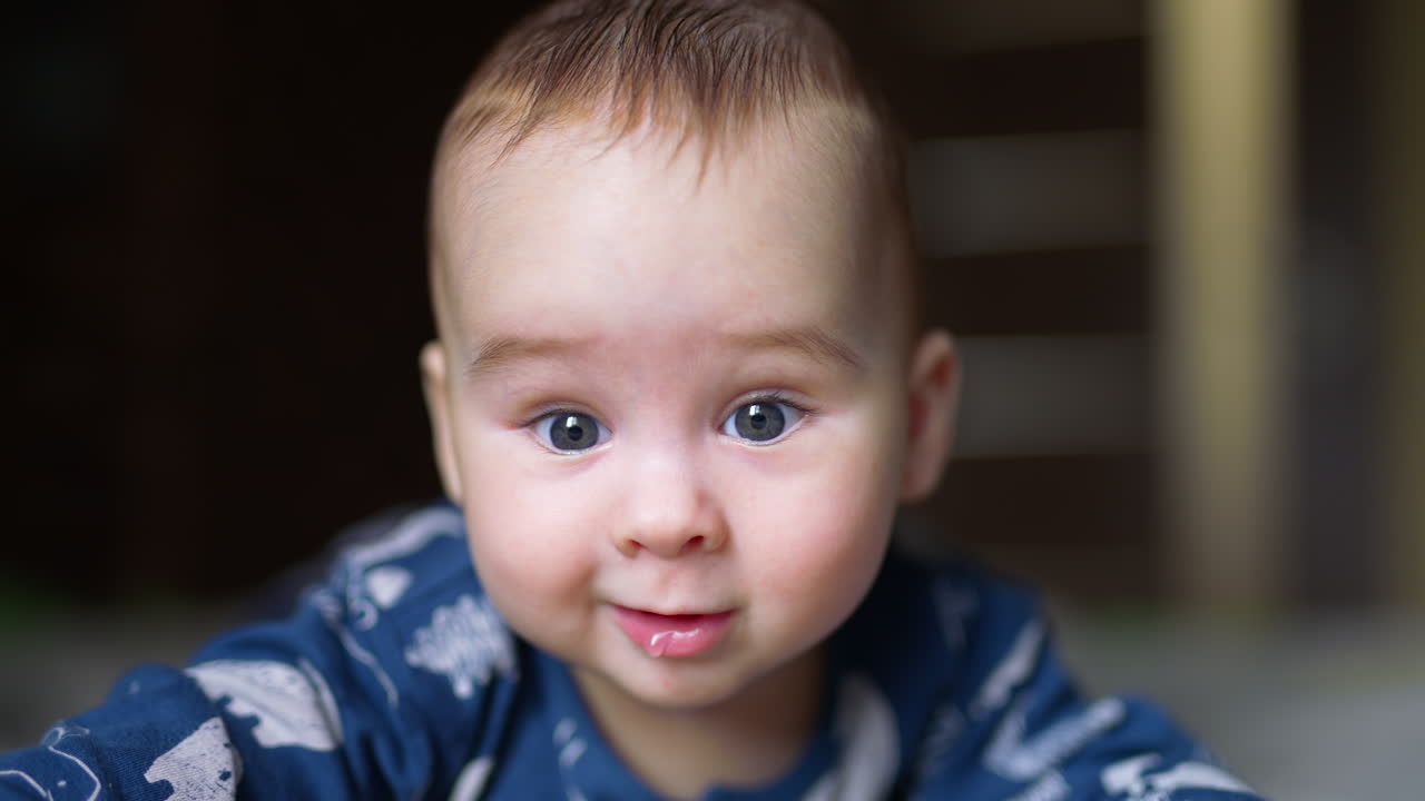 Face of an adorable toddler boy looking curiously into camera. Little baby smiling and saliva dripping from his mouth.