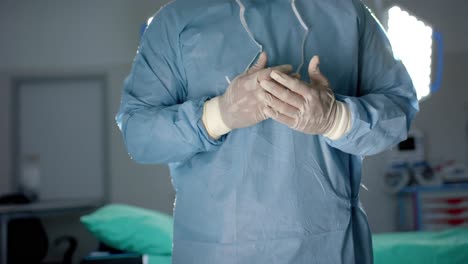 midsection of african american male surgeon wearing medical gloves in operating theatre, slow motion