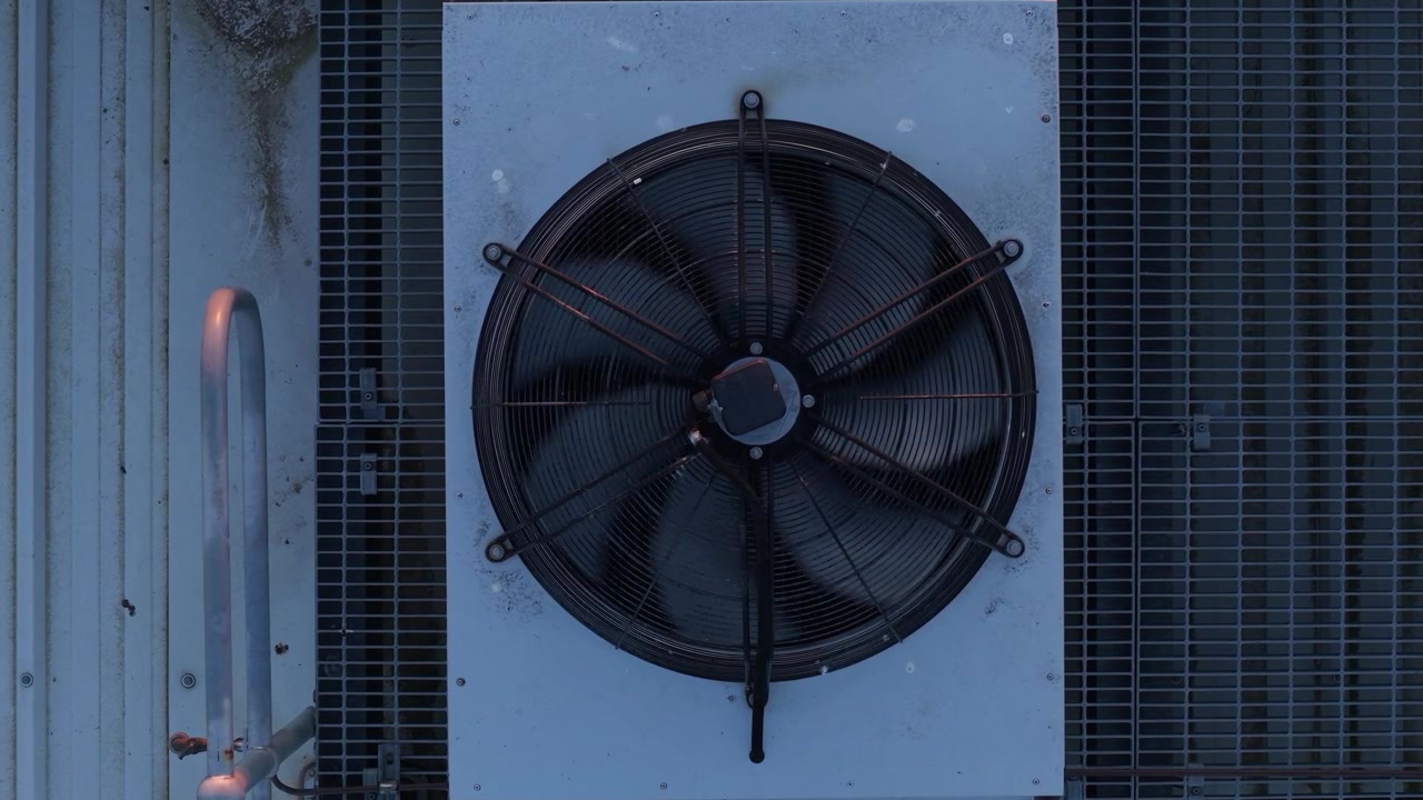 Close-up of a large, spinning fan on an external industrial air conditioning unit
