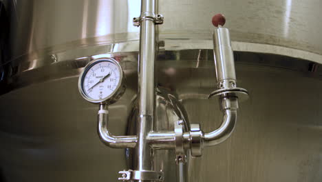 rack focus from a close-up of a pressure gauge and pipe mounted on a stainless steel fermentation tank in a brewery to a blurry view