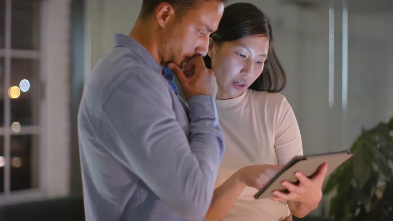 사무실에서 밤에 태블릿을 사용하고 이야기하는 다양한 남성과 여성 동료에 초점을 맞추었습니다.