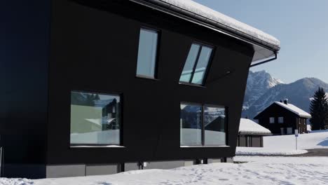 exterior of a contemporary black house with snow covered surroundings and a mountain range reflected in its windows. creating a striking contrast between modern architecture and the natural landscape