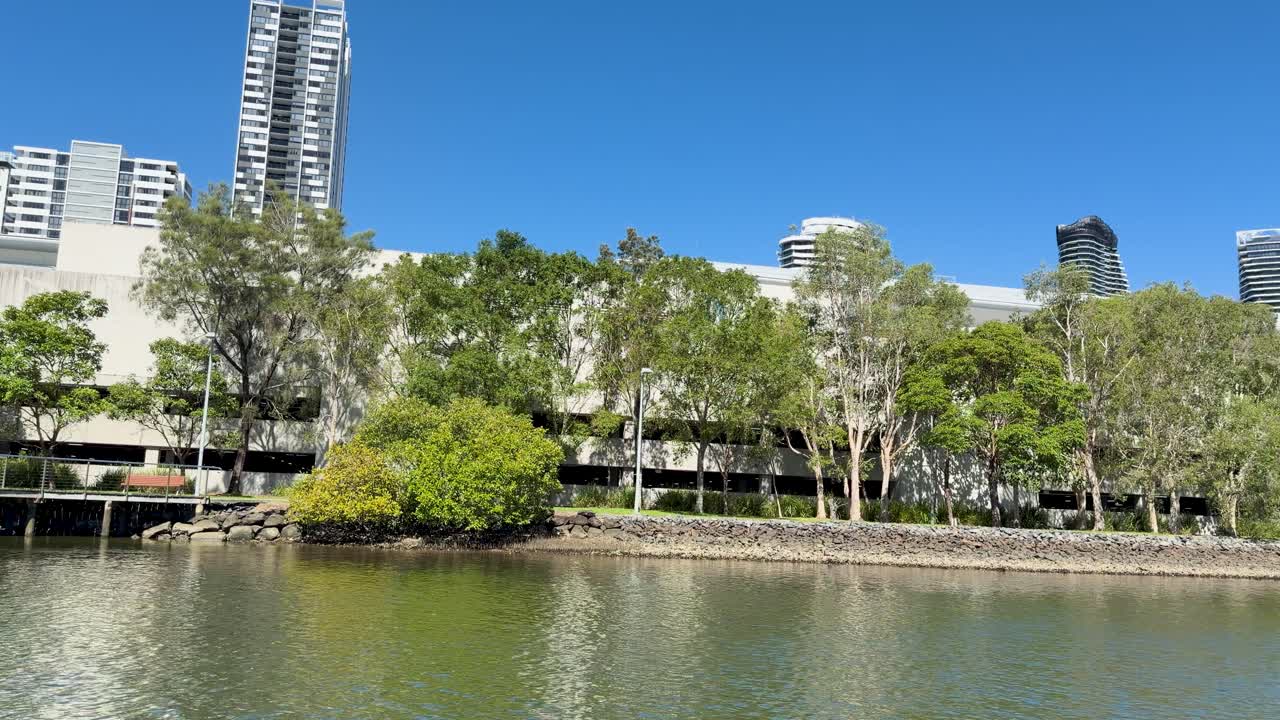 Smooth daytime pan along river, showing trees, skyscrapers, and bridge under clear blue sky