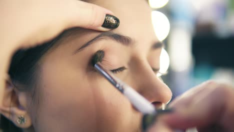 close up view of professional makeup artist hands using makeup brush to apply eye shadows. pro visagiste puts light brown shadows