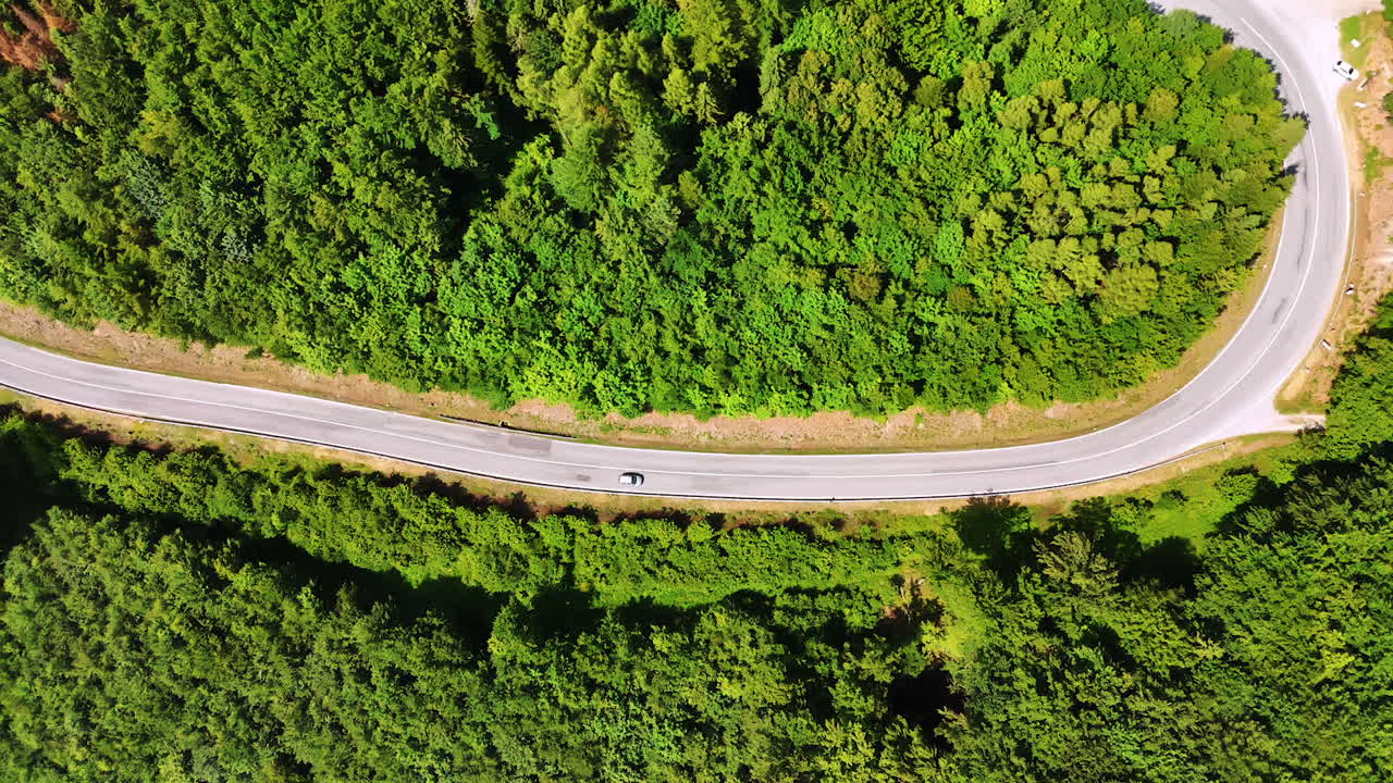 White car rides by the wavy highway in the woods. Drone footage over the nature in the countryside of Slovakia