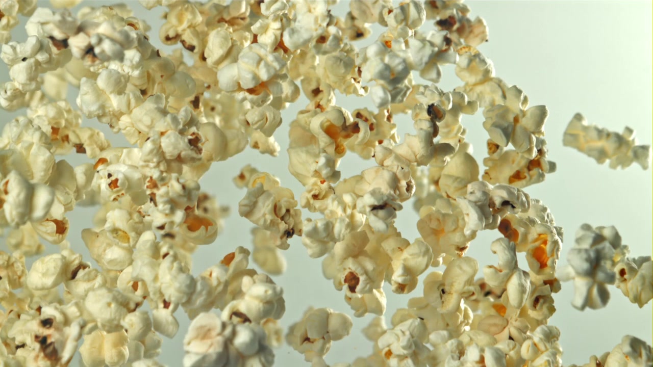 Palomitas de maíz volando y cayendo en cámara lenta sobre fondo blanco
