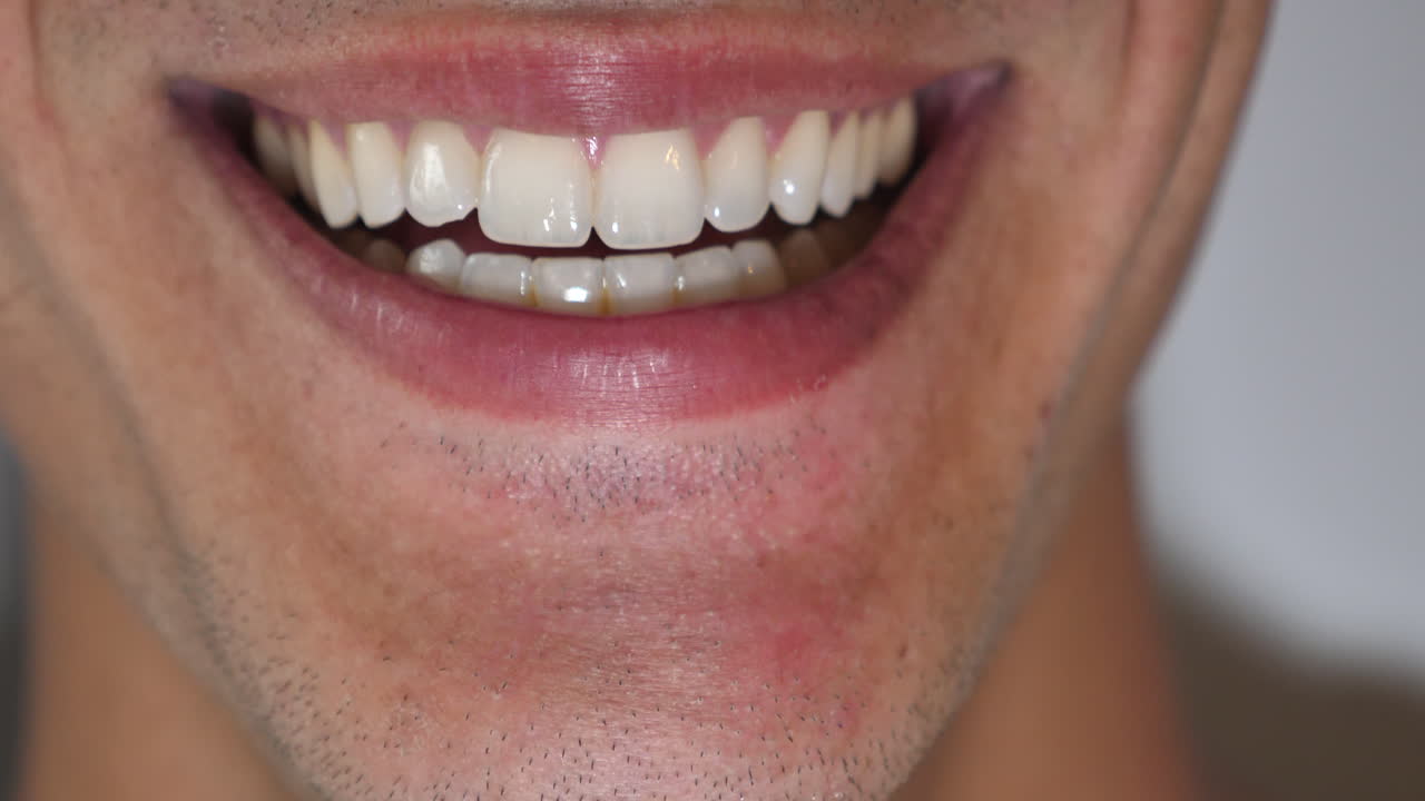 un primerísimo plano masculino limpio y afeitado de dientes blancos y rectos, lamiendo los labios y sonriendo a la cámara