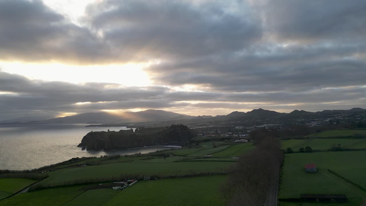 Dramatic Sunset over Coastal Landscape with Green Fields and Mountains