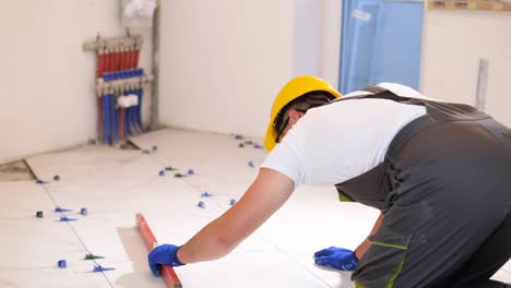 a builder measures the level of the floor a worker during the laying of ceramic tiles