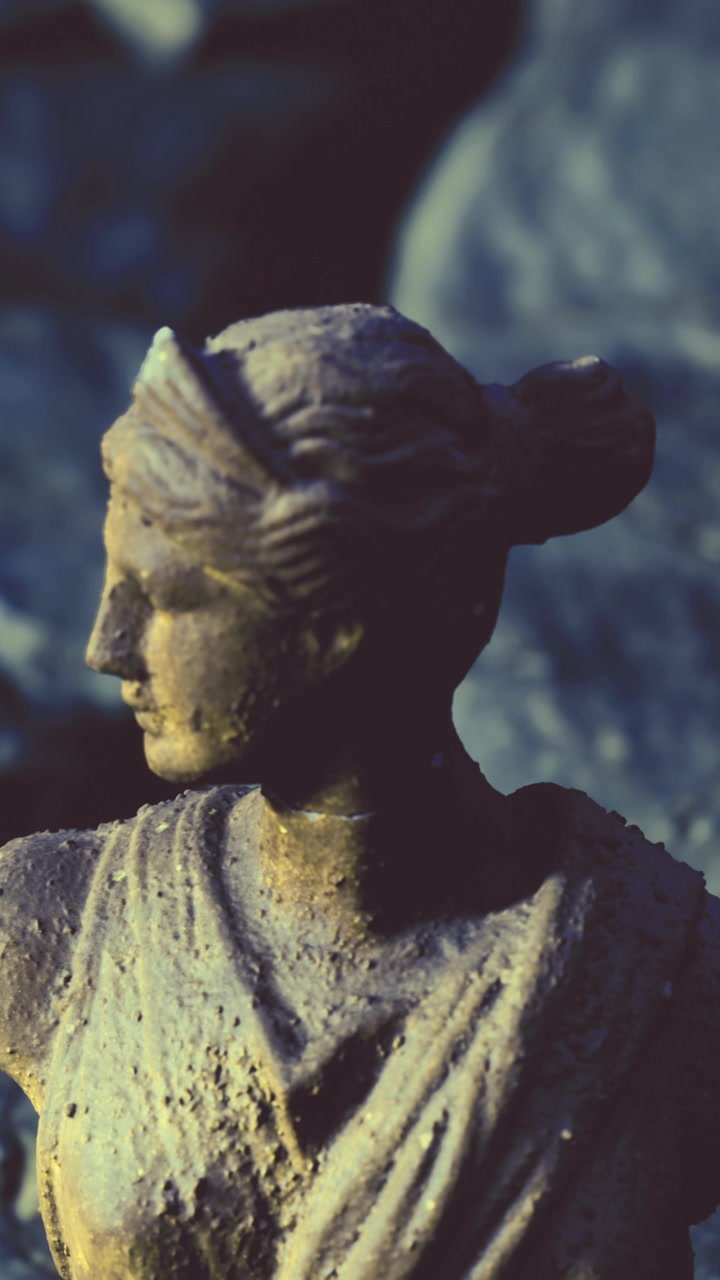 Statua di una donna con acconciatura a chignon posizionata tra le rocce all'aperto.