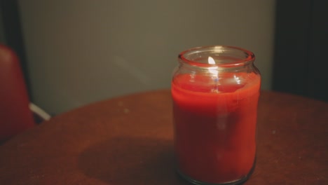 Close-Up-View-Of-A-Candle-Inside-A-Glass-Illuminating-A-Dark-Scene-And-Reflections-On-Wooden-Table---high-angle,-static-shot