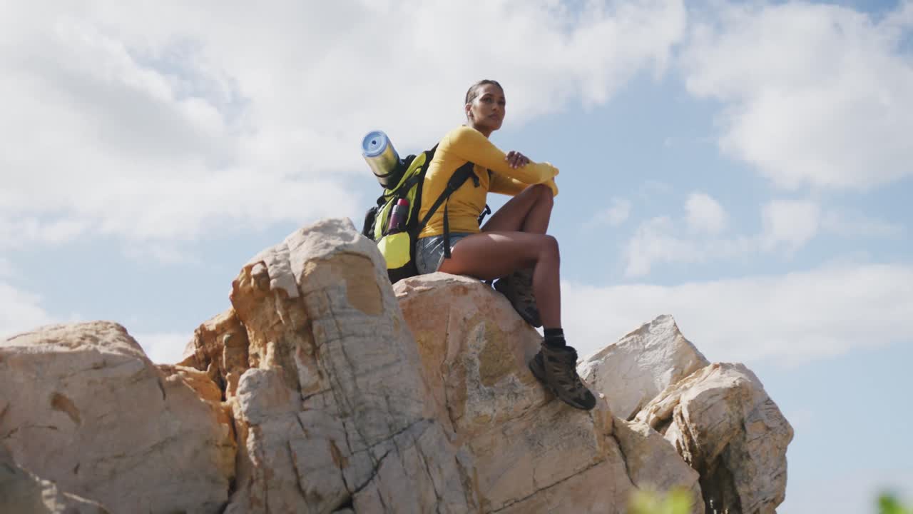 African american woman with backpack enjoying the view sitting on the rocks while hiking