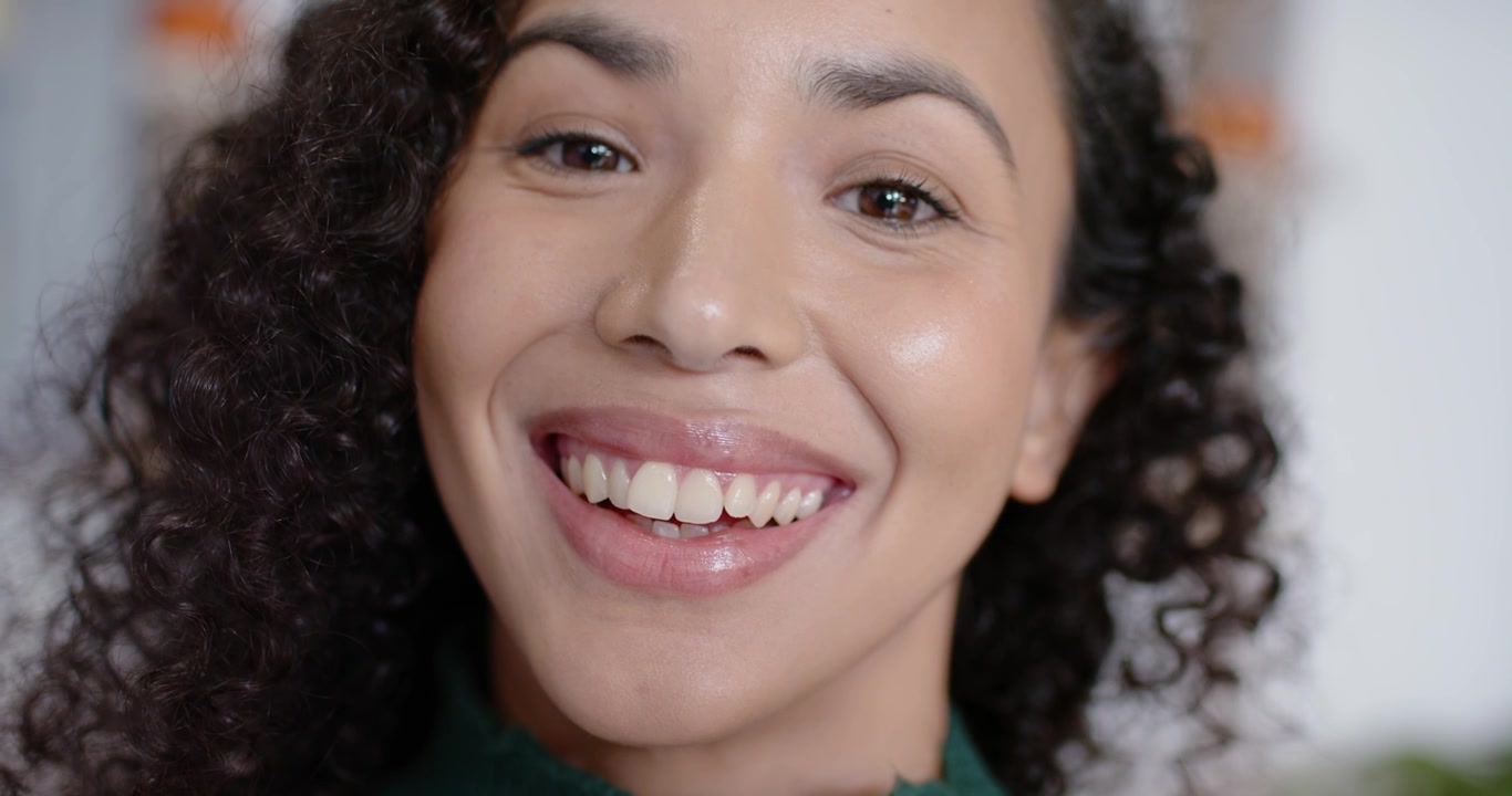 Mulher afro-americana sorrindo gradualmente após sinal da câmera, vestindo suéter verde em casa