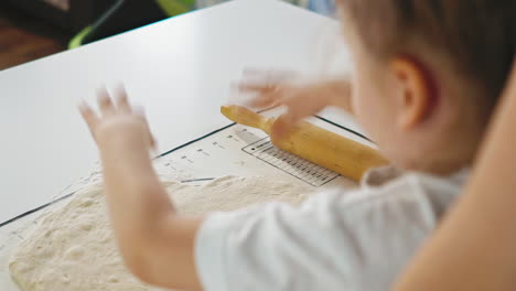 child takes flour working with dough at table in kitchen