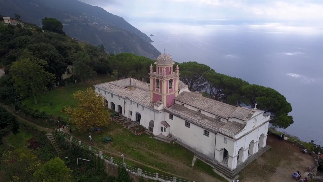 Vista aerea con drone della chiesa bianca del Santuario di Montenero con dettagli rosa, appollaiata su una scogliera a picco sul mare a Riomaggiore, Cinque Terre, Italia