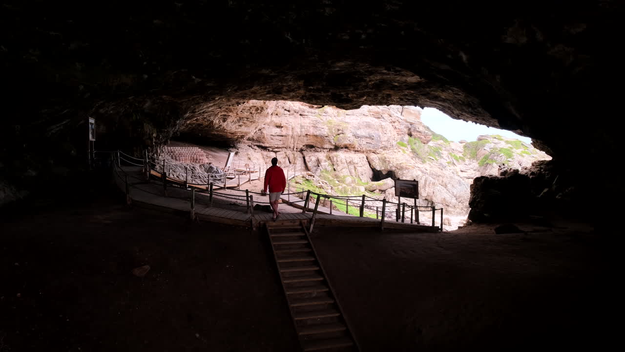 Interior view of dark Klipgat Cave as male traveler explores on boardwalk