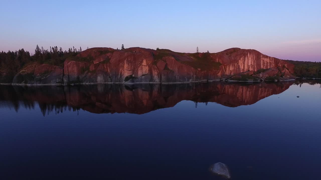 Alpinista escalando um penhasco acidentado acima de um lago calmo na hora dourada perto de Peggys Cove Loop em Nova Scotia, Canadá