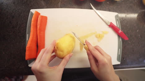 Mujer-Pelando-Patatas-En-La-Cocina-A-Cámara-Lenta,-Vista-Superior