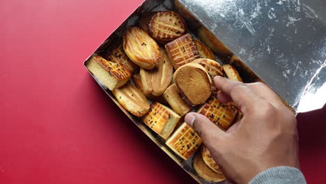 a hand reaching for a cookie from a box of assorted cookies