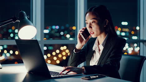Businesswoman working on laptop and talking on phone at night