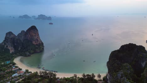 railay beach with traditional longtail boats dotting the andaman sea, surrounded by towering limestone cliffs at sunrise, krabi, thailand. lovely aerial view flight panorama overview drone