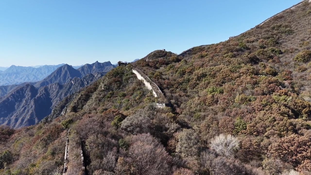 Ripresa aerea su un paesaggio montuoso roccioso con la Grande Muraglia visibile su un crinale distante, terreno autunnale spoglio in primo piano e cime blu sullo sfondo, Distretto di Huairou, Pechino, Cina