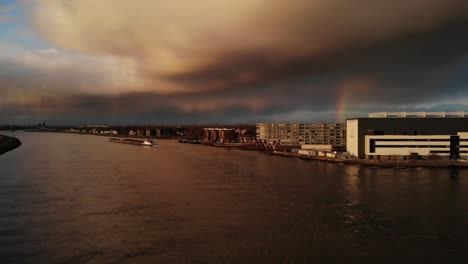 Dramatic-sky-over-Noord-river-as-long-container-ship-sails-down-river