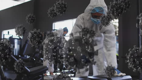 multiple covid-19 cells floating over group of health workers cleaning the gym using disinfectant