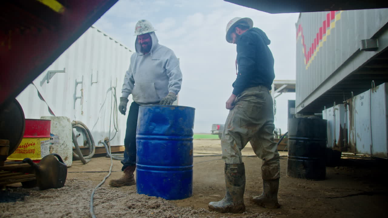 Man lift and turn the heavy blue barrel. People working at the site for oil production. Low angle view.