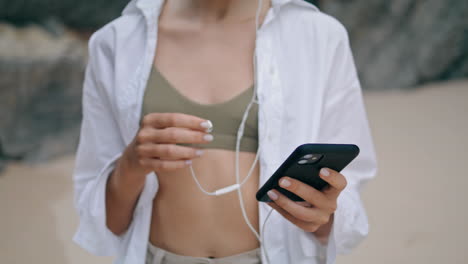 Niña-Poniendo-Auriculares-En-La-Playa-De-Cerca.-Mujer-Activando-La-Aplicación-Móvil.