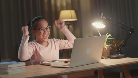 young asia girl student celebrating with laptop computer at home, teenage girl learning online from laptop at night