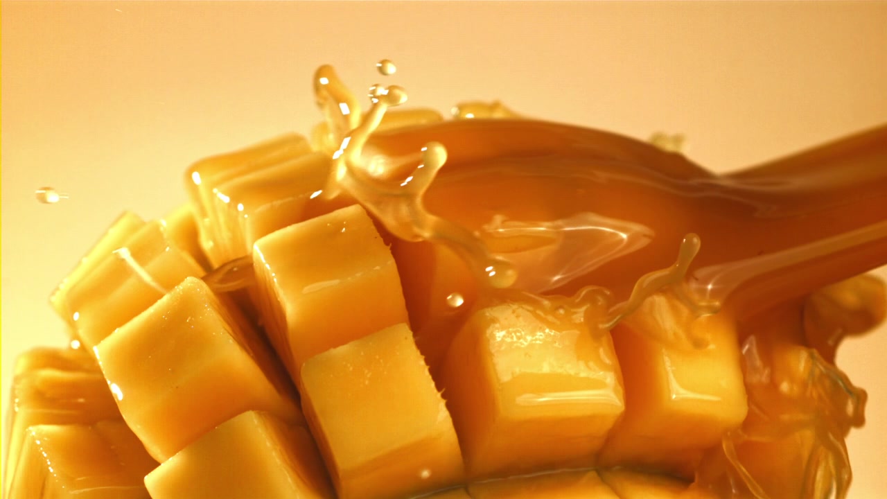 Sciroppo dorato che cola su cubetti di mango fresco tagliato a dadini al rallentatore.
