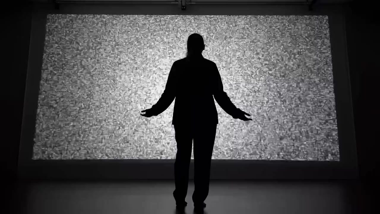 Solitary silhouette standing centered before large static filled projection with open palms, settling posture, and dramatic backlit contrast inside dark studio gallery space