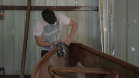 A-young-male-carpenter-hand-sanding-the-plywood-bow-of-a-canoe