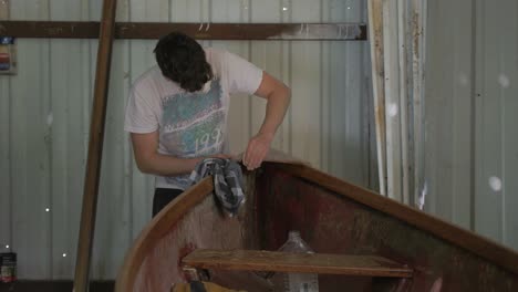 a young male carpenter hand sanding the plywood bow of a canoe