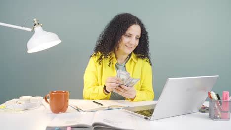 mujer joven mirando la computadora portátil contando dinero.