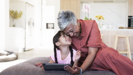 Abuela-Birracial-Se-Ríe-Con-Una-Nieta-Birracial-Sosteniendo-Una-Tableta,-Con-Espacio-Para-Copiar