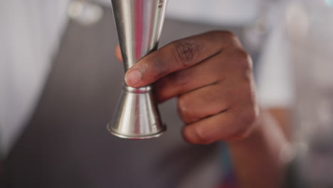 barman pours juice into jigger in bar closeup. black bartender measures ingredient for refreshing cocktail in club. barkeeper makes exotic drink