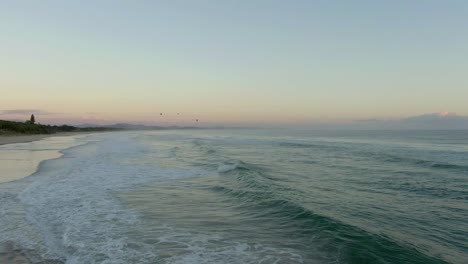 Vuelo-De-Drones-A-Baja-Altitud-Sobre-La-Playa-De-Byron-Bay-Australia,-Drones-Avanzando-Hacia-Tres-Globos-Aerostáticos-Que-Vuelan-Sobre-El-Mar