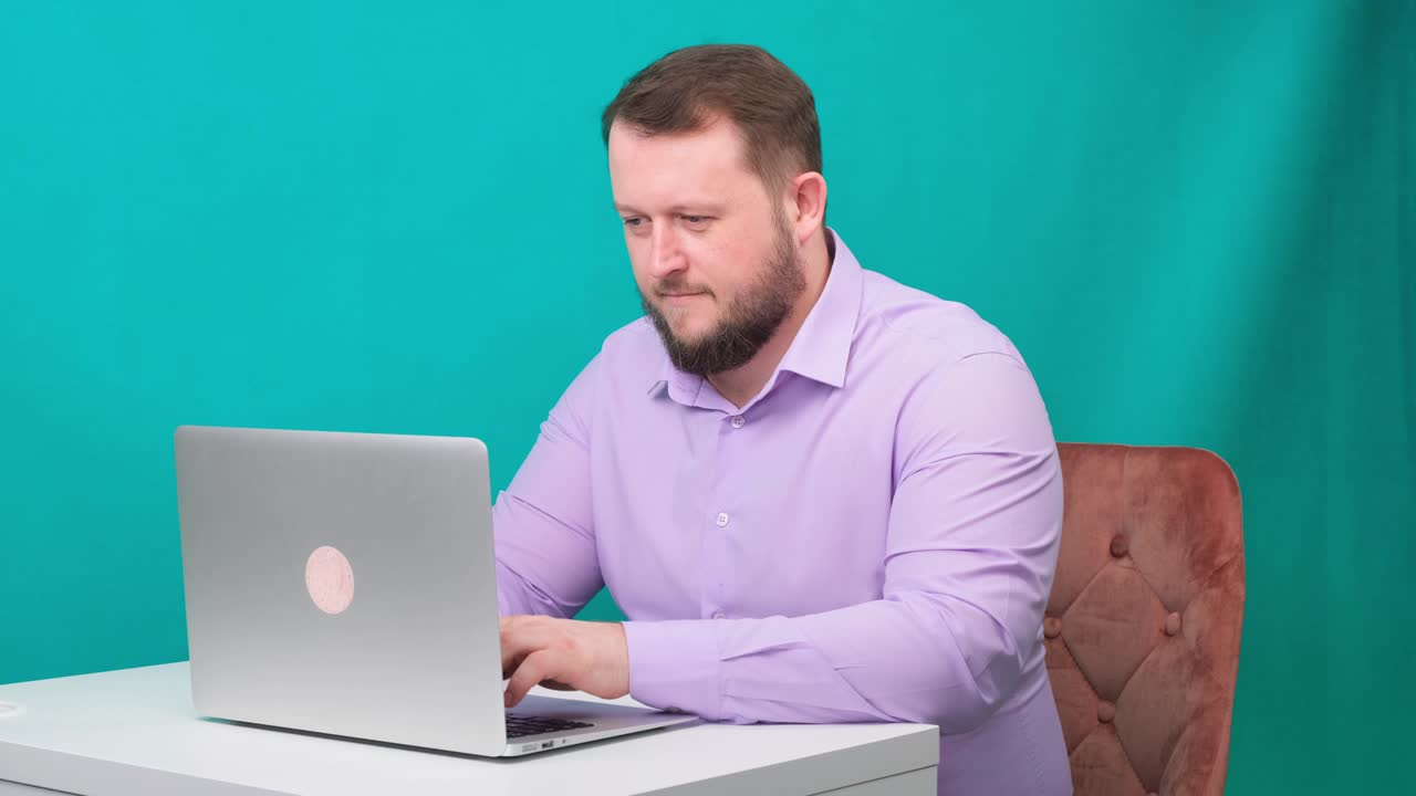 젊은 행복한 사업가가 녹색 스크린에서 노트북으로 타이핑하고 있습니다. 노트북을 바라보는 남성 이야기하는 남자의 초상화. 사무실에서 그의 책상에서 일하는 남자