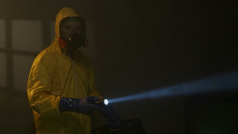 hombre vestido con traje de materiales peligrosos explora una habitación llena de humo