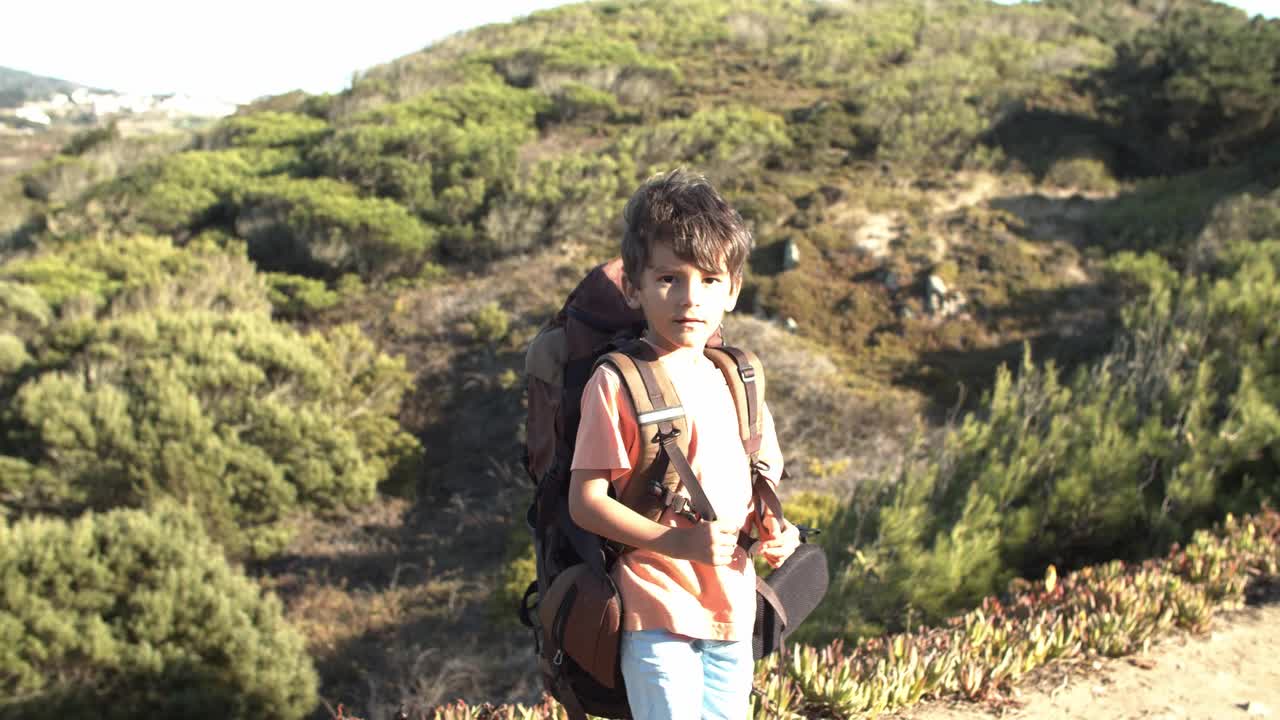 niño lindo caminando por el camino de la montaña, llevando una mochila grande
