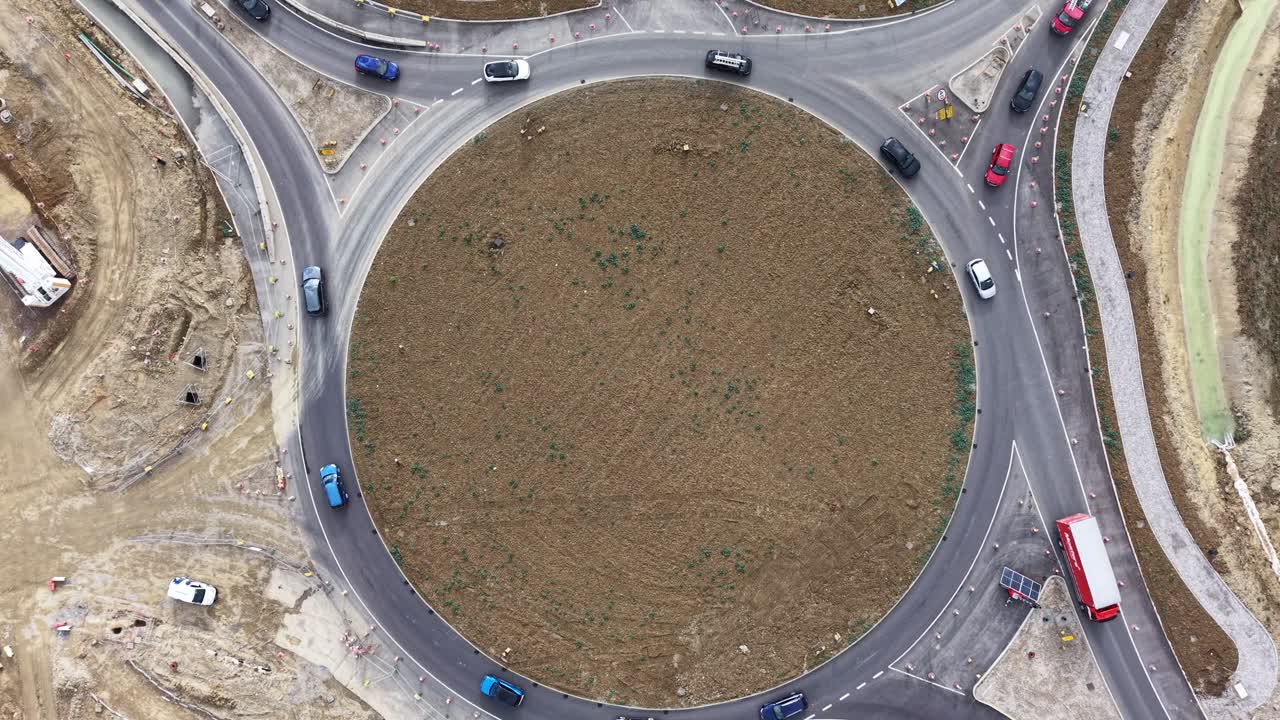 Overhead 4K aerial drone footage of vehicles navigating a busy roundabout in the United Kingdom. The clip captures dynamic traffic movement, road layout,a bird’s-eye perspective