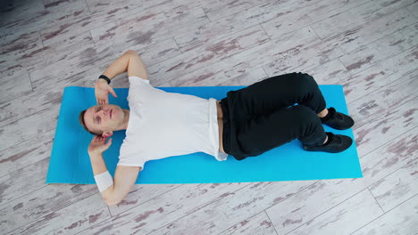 man training at home. keeping fit. young man in white t-shirt and black pants doing workout on a mat. sport and health. top view.