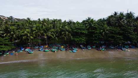 Aerial-dolly-left-shot-of-beach-scene-with-people-and-their-coracle-boats-on-sand
