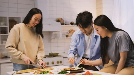 tres amigos japoneses sentados alrededor del mostrador de la cocina cortando y comiendo sushi 3