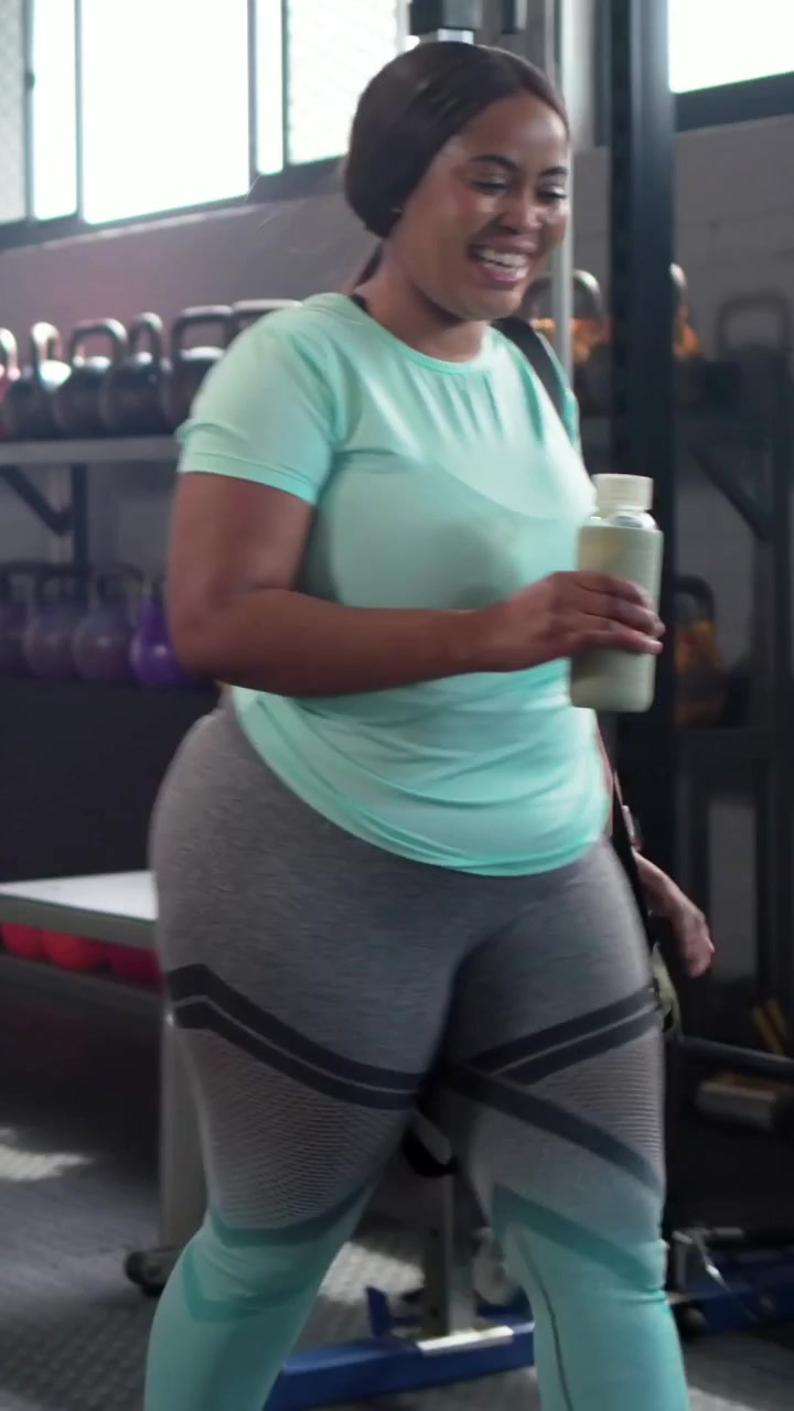 Video verticale: Due donne con top rosa e verde menta entrano in palestra, trasportando un borsone e un asciugamano, mentre si riscaldano.