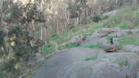 Aerial-shot-orbiting-around-a-little-boy-sitting-on-a-bolder-on-a-hill-in-the-middle-of-the-Australian-bush