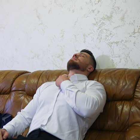 young handsome man in white shirt rests on a sofa in a hotel room. businessman moved in a hotel during business trip. modern hotel interior